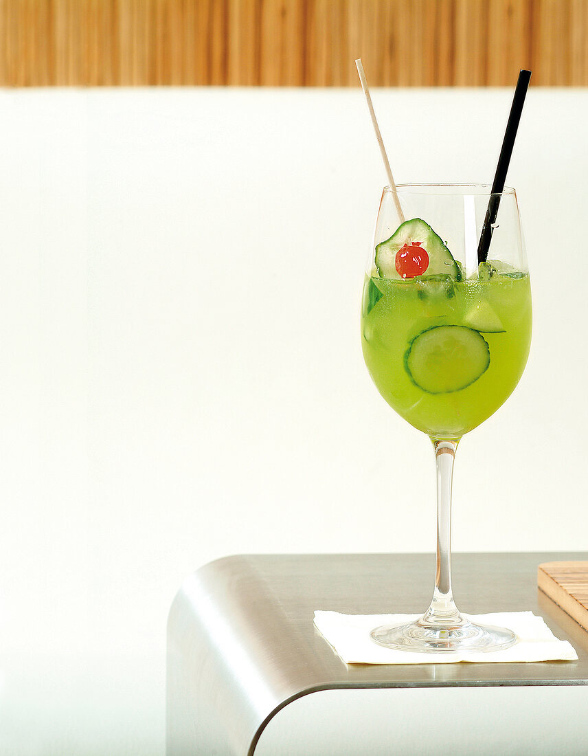 Glass of cocktail with cucumber slices and cherry