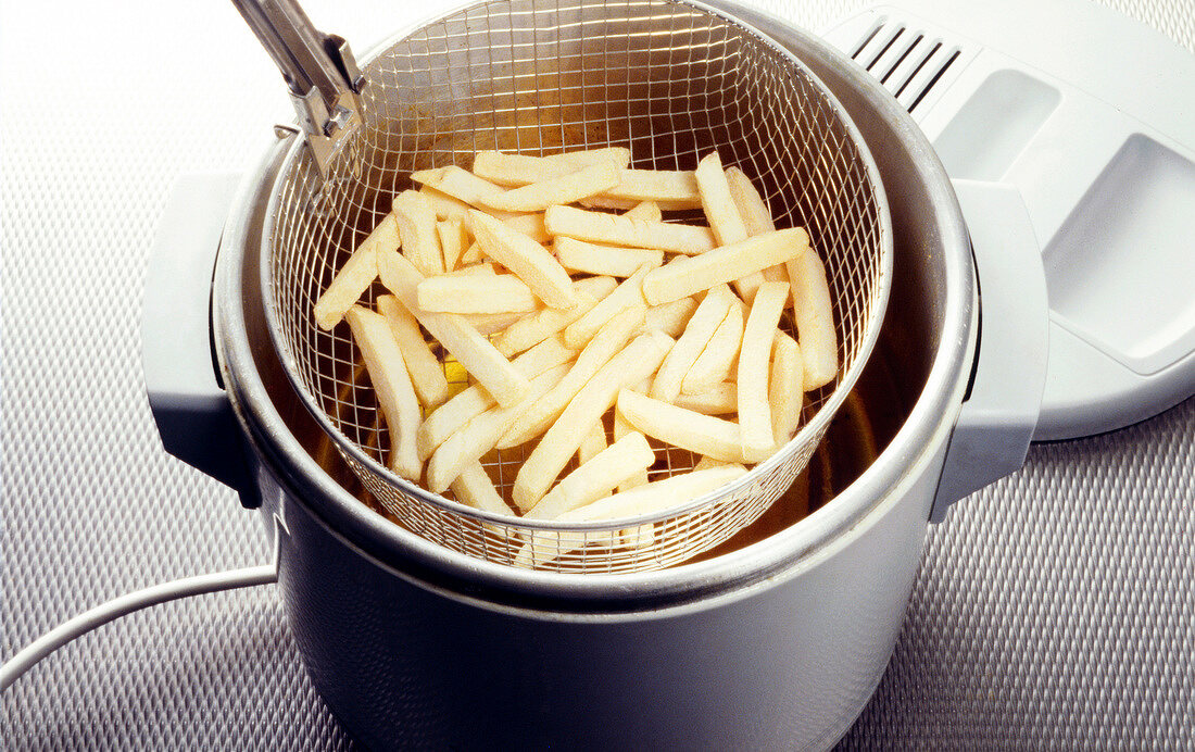 Potato fries being put into the fryer with strainer