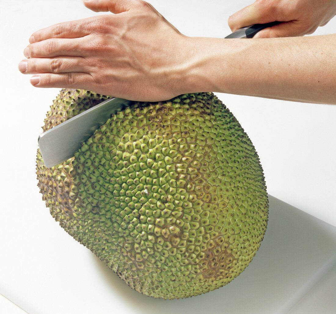 Close-up of hands cutting jackfruit with cleaver, step 1