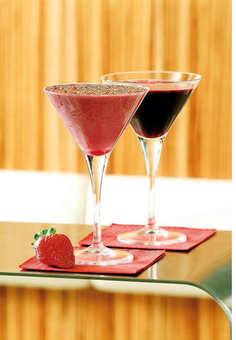 Zwei verschiedene Cocktails in Martinigläsern, davor eine Erdbeere