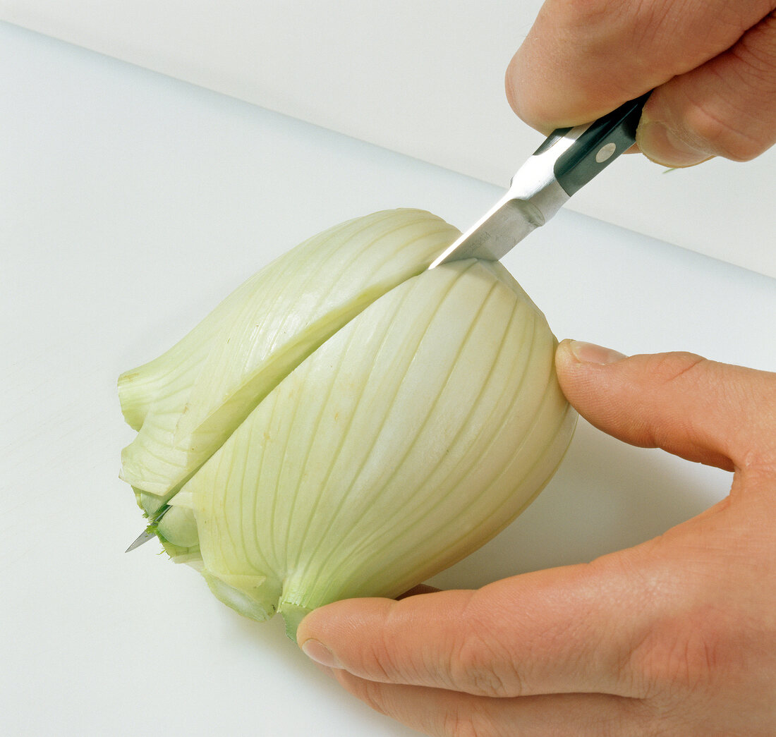 Close-up of hands cutting fennel bulb into halves, step 2