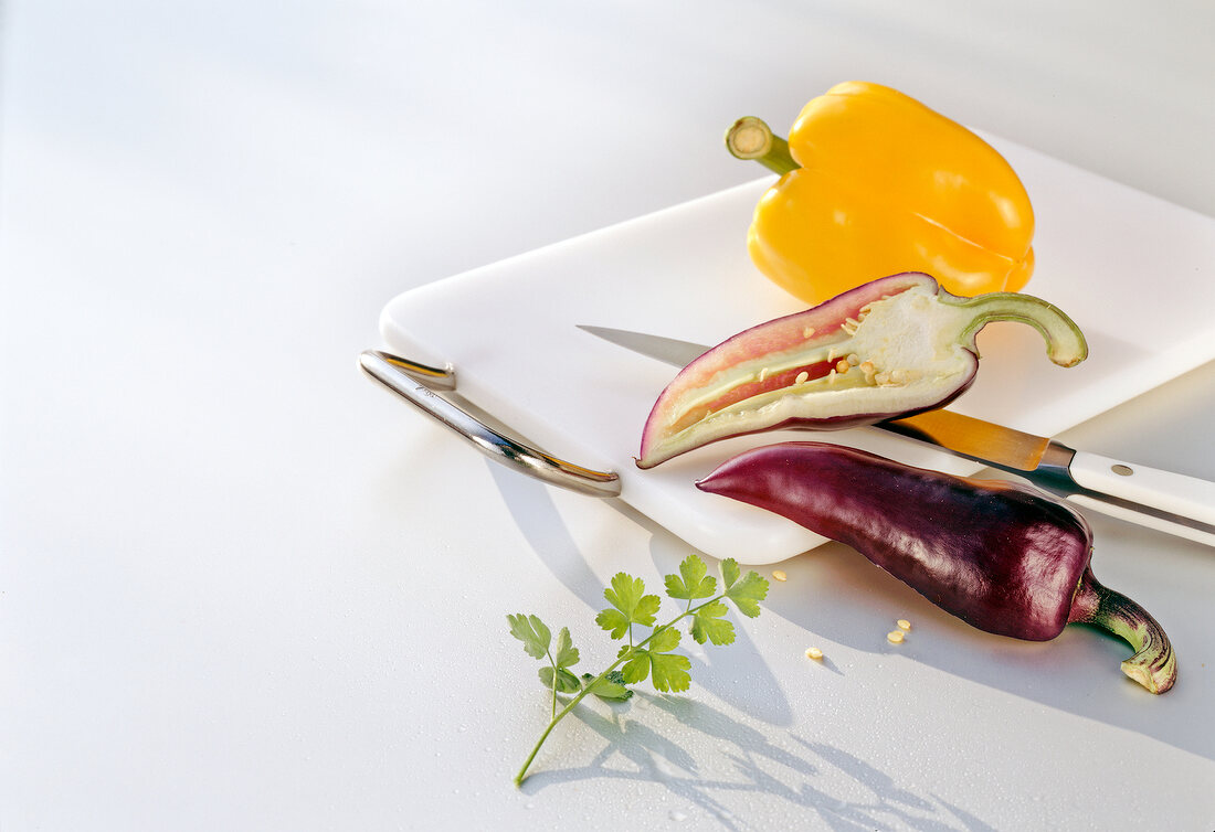 Yellow and purple pepper with knife and chopping board on white background