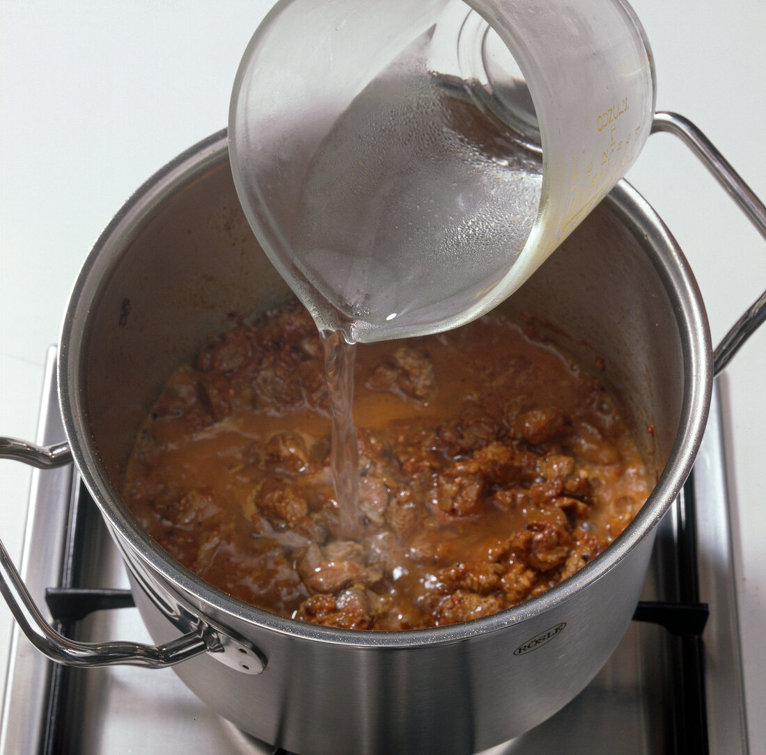 Close-up of adding water to meat and onions while preparing goulash soup, step 5