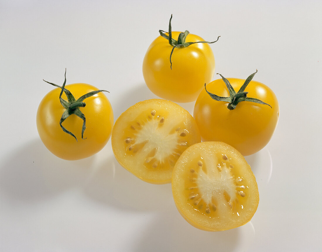 Whole and halved yellow round tomatoes on white background
