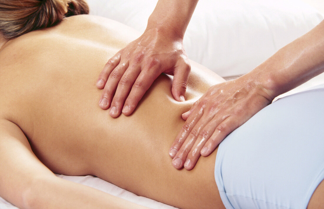 Woman receiving on her lower back from masseur with thumbs, relaxing