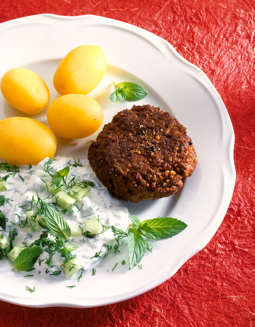 Close-up of meatball with boiled potatoes and cheese cream on serving dish