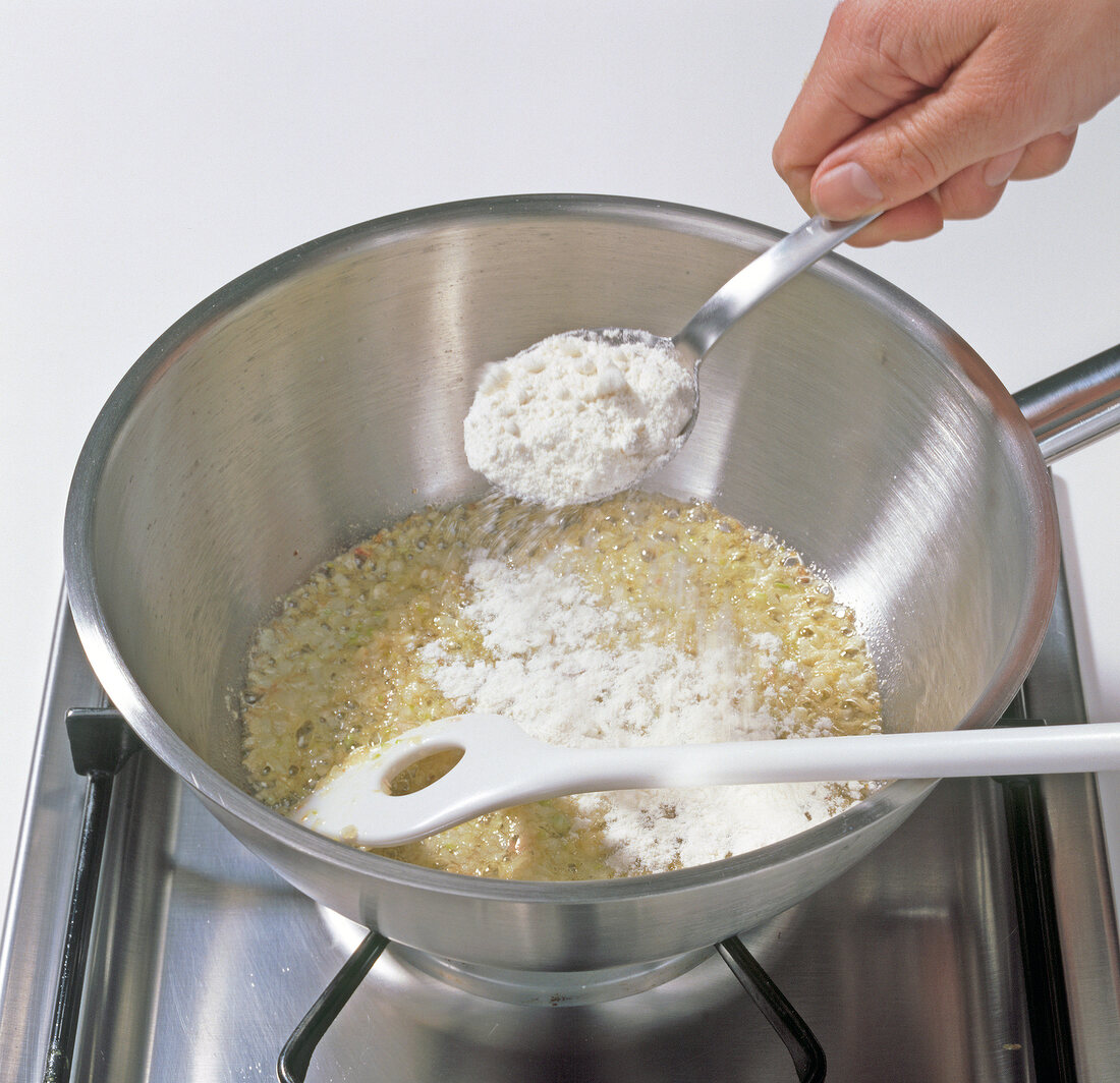 Close-up of adding flour to butter and shallots in pot, step 1