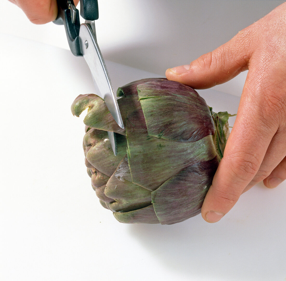 Close-up of hands cutting leaves of artichoke by scissors, step 3