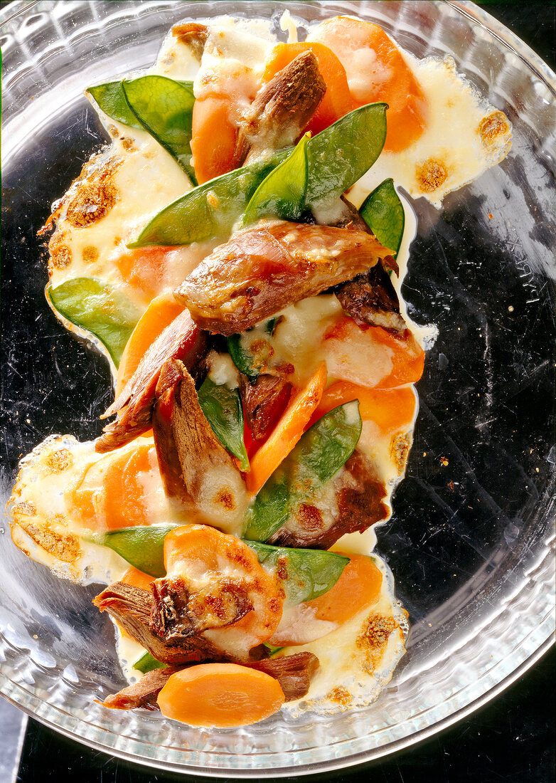 Close-up of gratin with goose meat and vegetables on glass plate