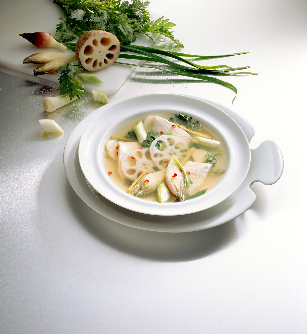Asian vegetable soup with lotus root in serving dish on white background