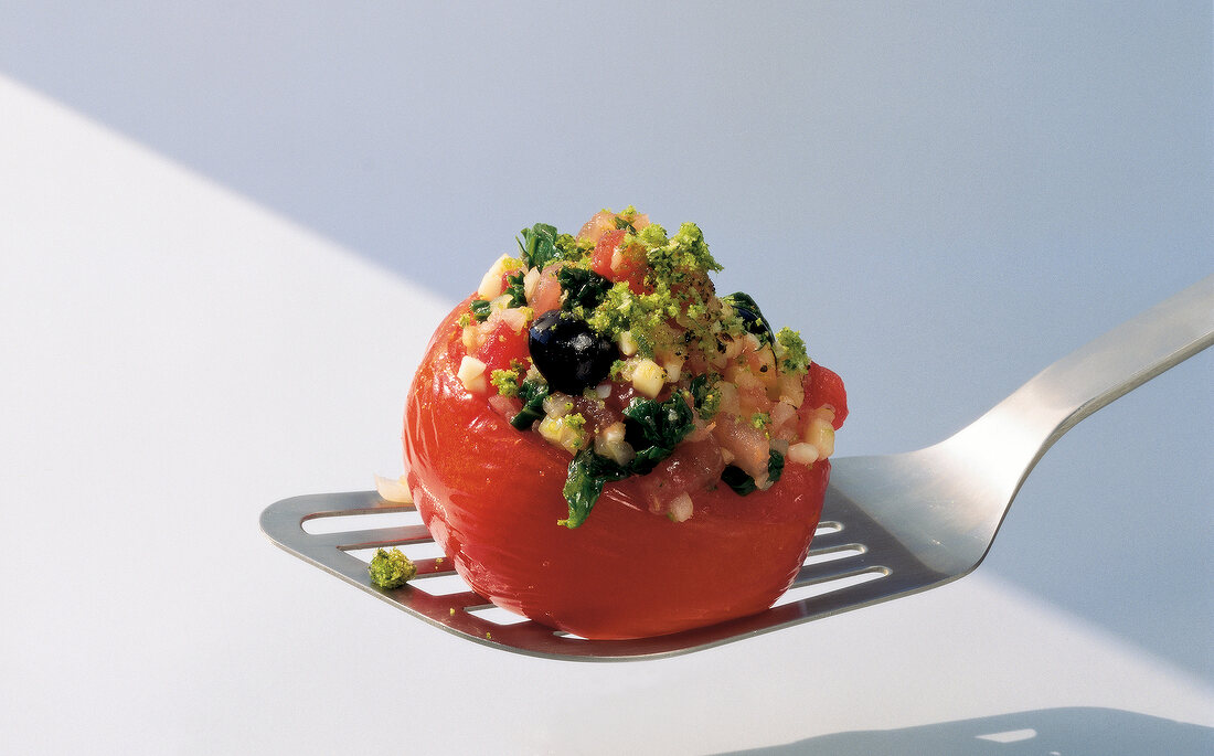 Stuffed tomato with black olives and parsley on spatula