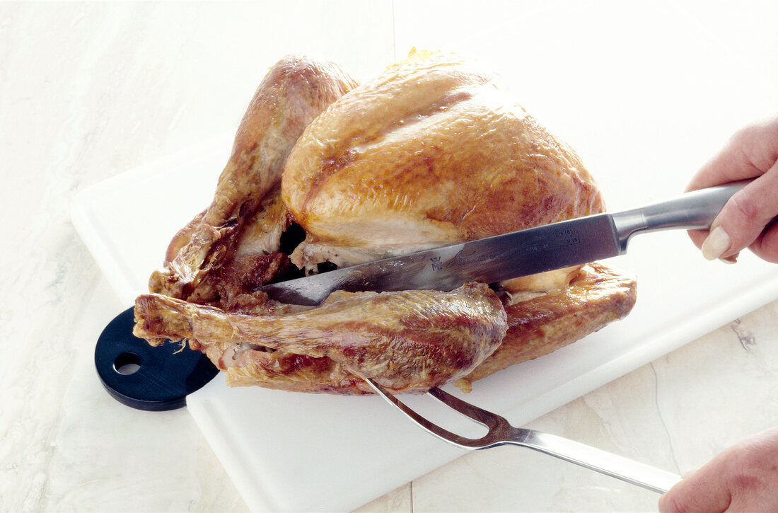 Baked chicken being cut with knife and carving fork on chopping board, step 1