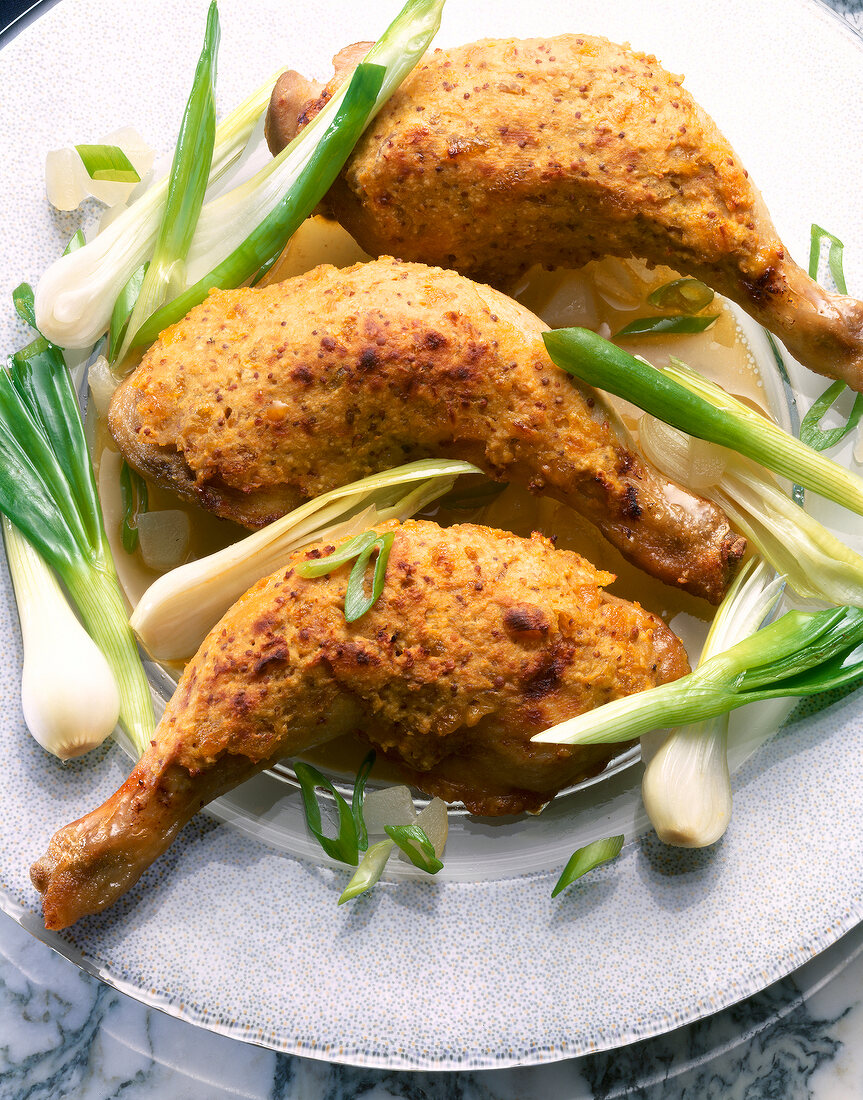 Close-up of chicken legs with mustard crust and green onions on plate