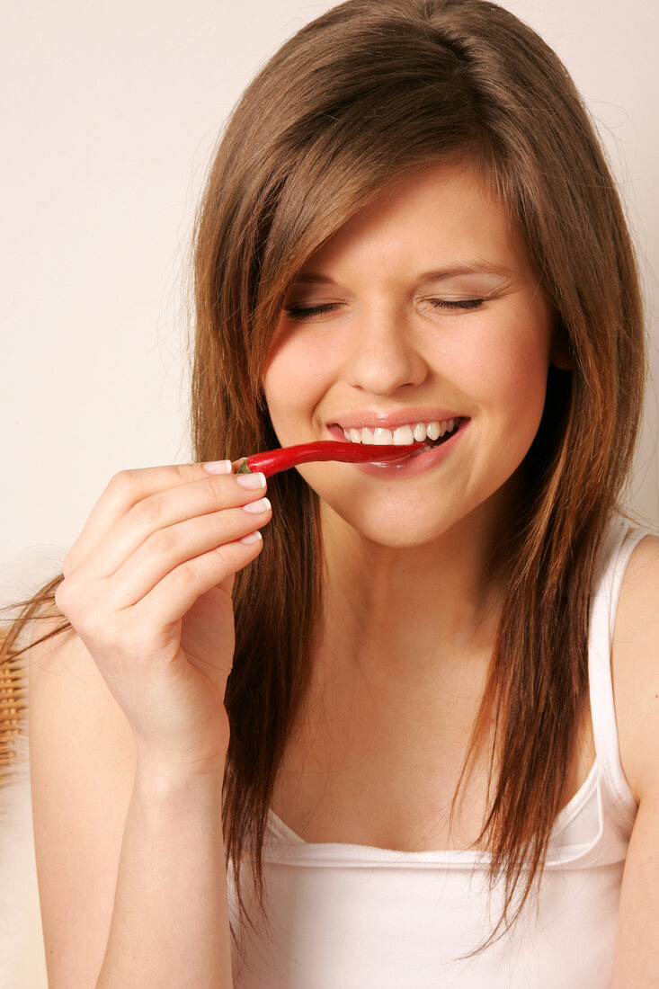 Frau mit langen Haaren und Augen zu beißt in rote Peperoni