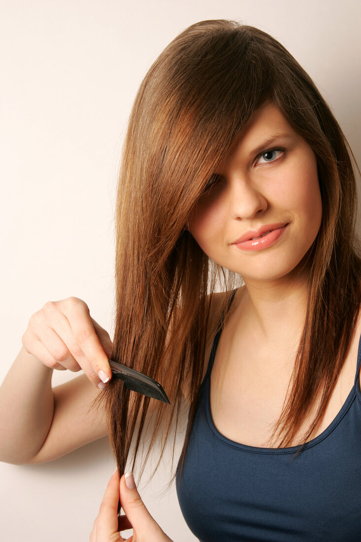 Portrait of pretty woman with brown hair wearing blue top combing her hair, smiling