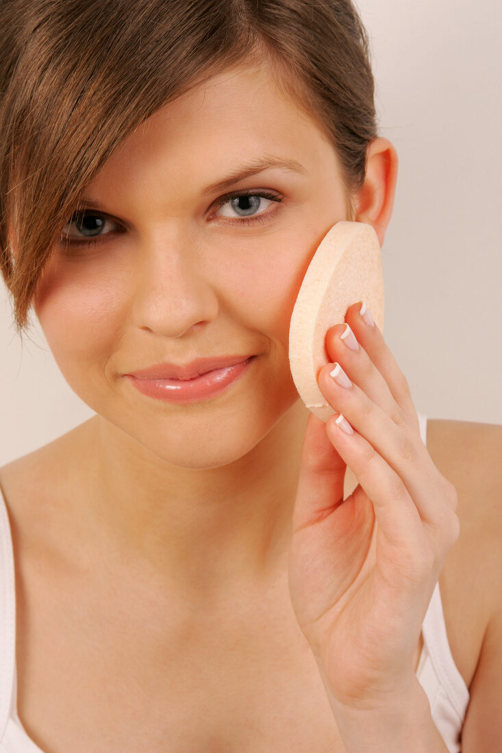 Portrait of pretty woman with brown hair cleaning her face with pad