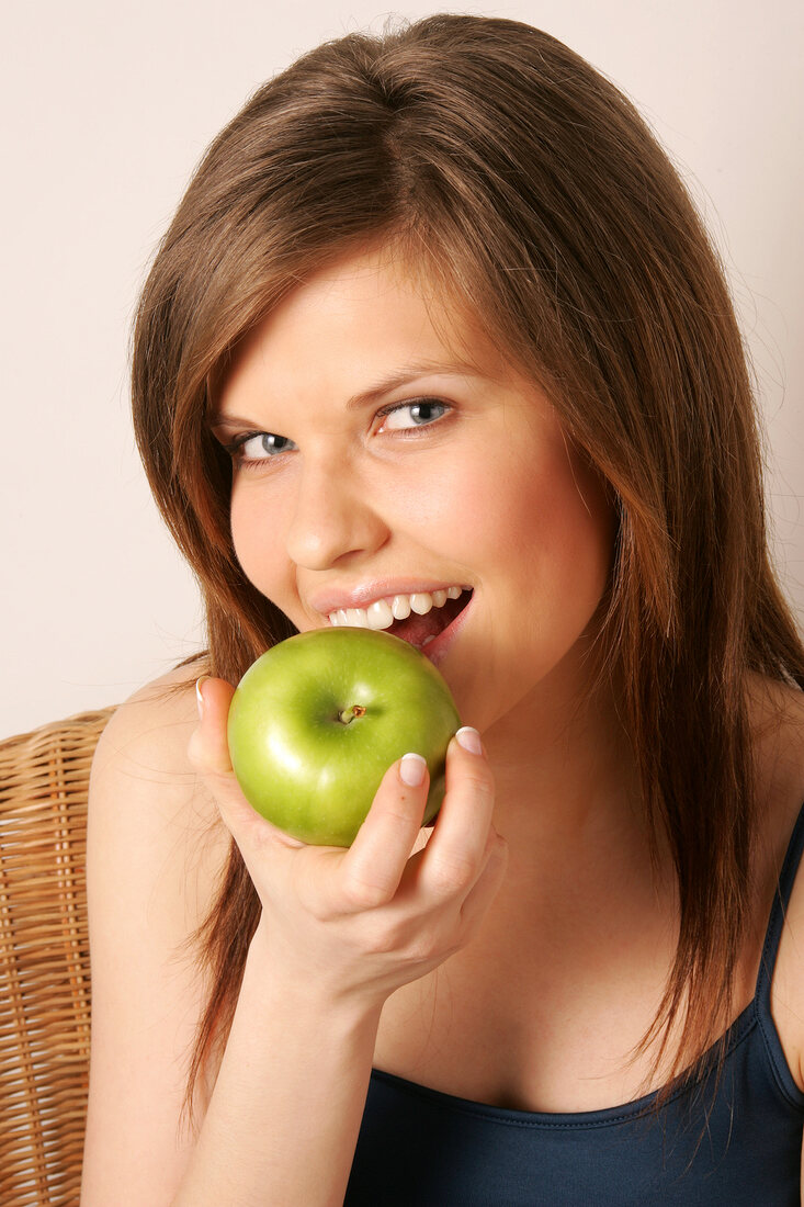 Portrait of woman with long hair holding green apple, smiling