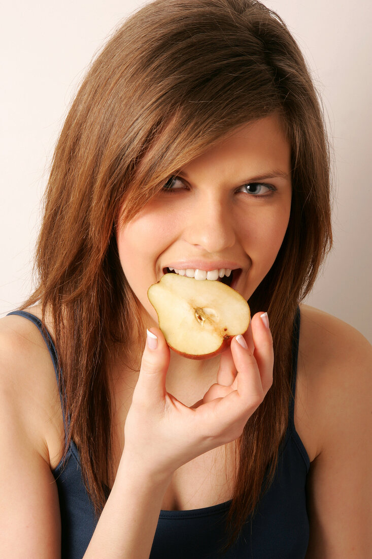 Portrait of woman with brown hair eating half red pear