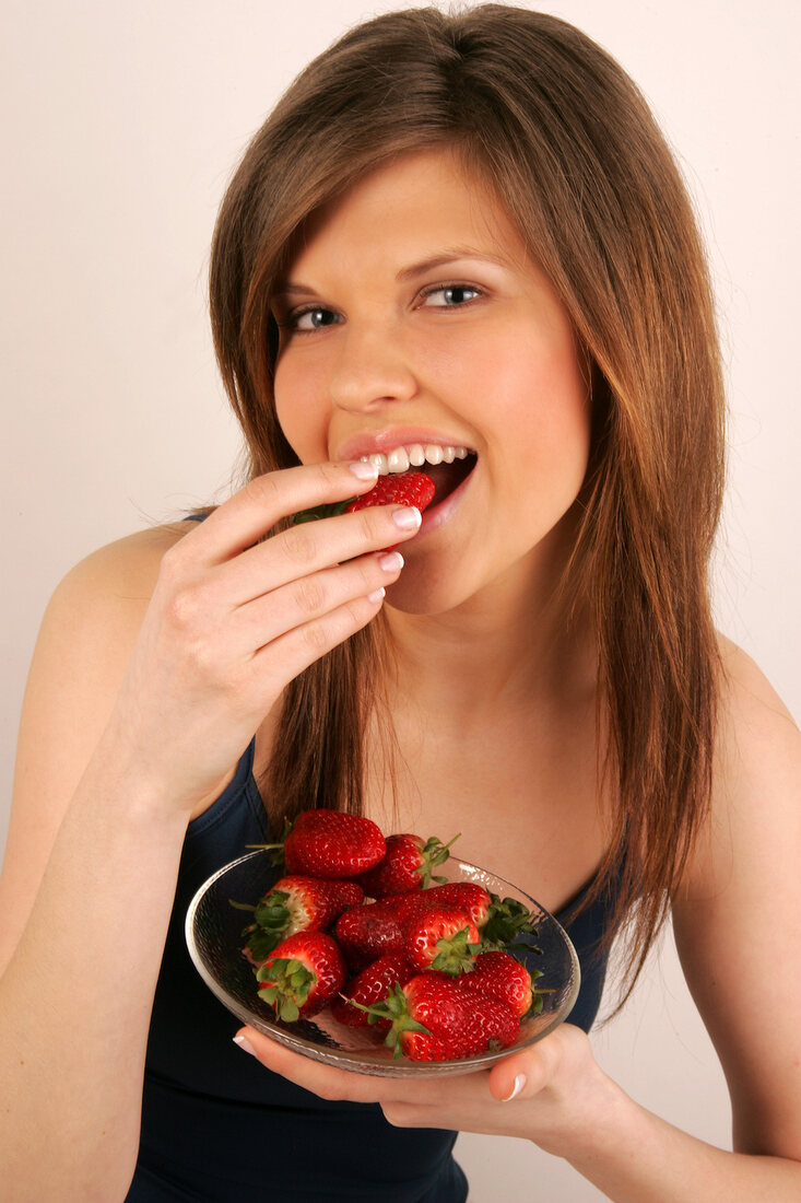 Portrait of woman with brown hair biting strawberry while holding plate of strawberries