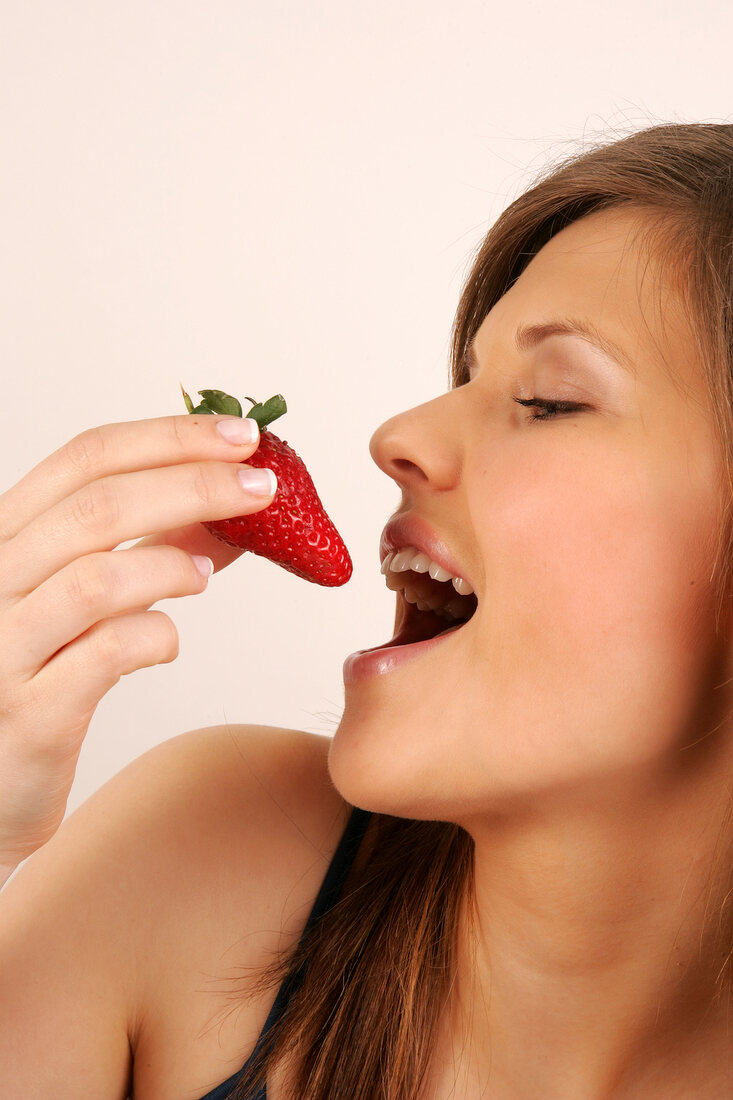 Frau mit langen Haaren isst Erdbeere mit Hand, Detail