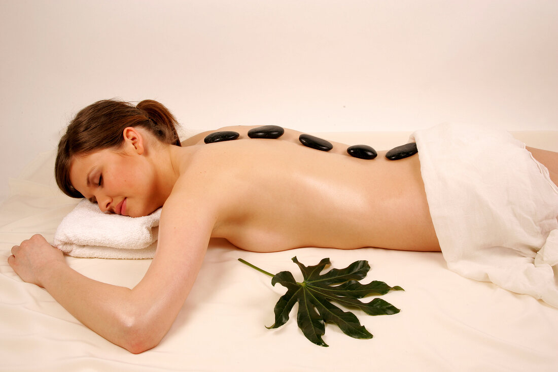 Rear view of semi nude woman lying with stones on her back