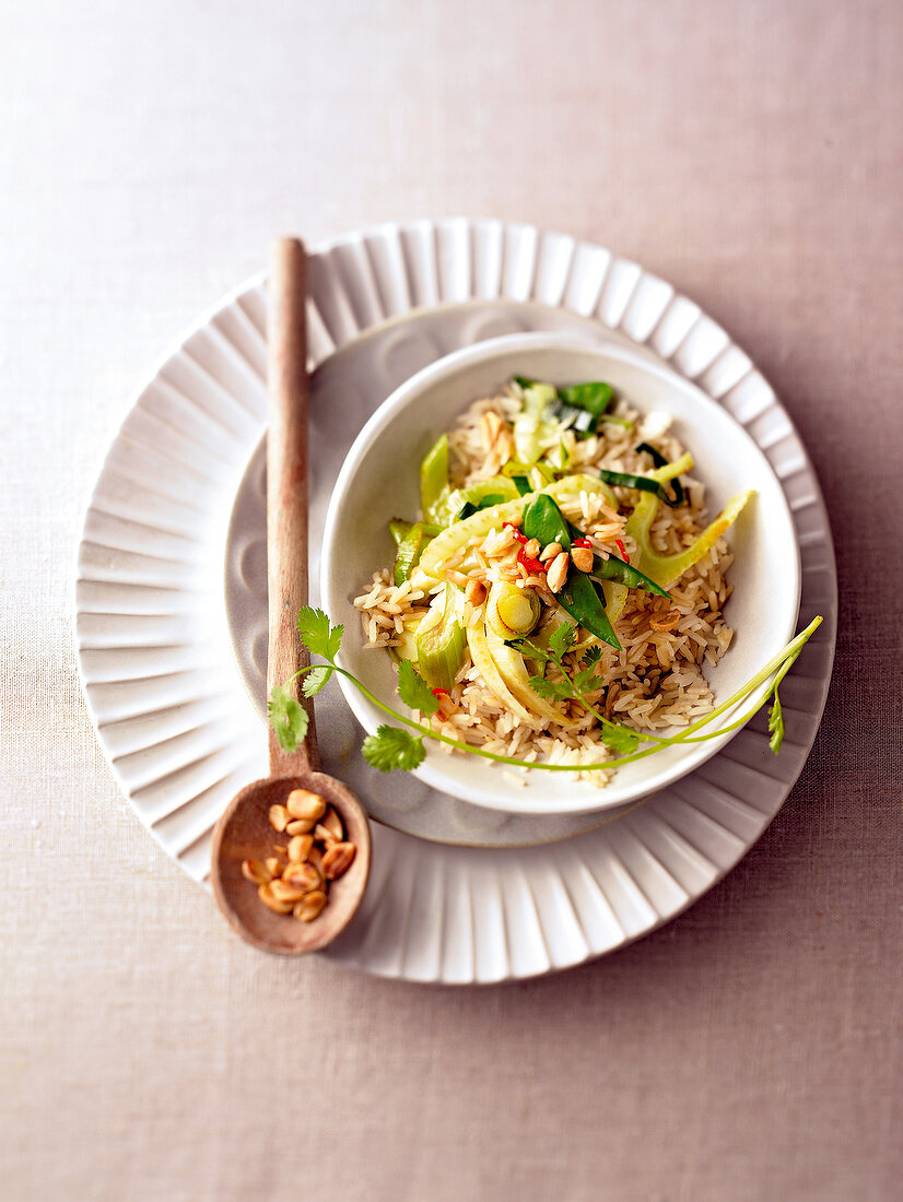 Fried rice with vegetables in bowl and wooden spoon on plate