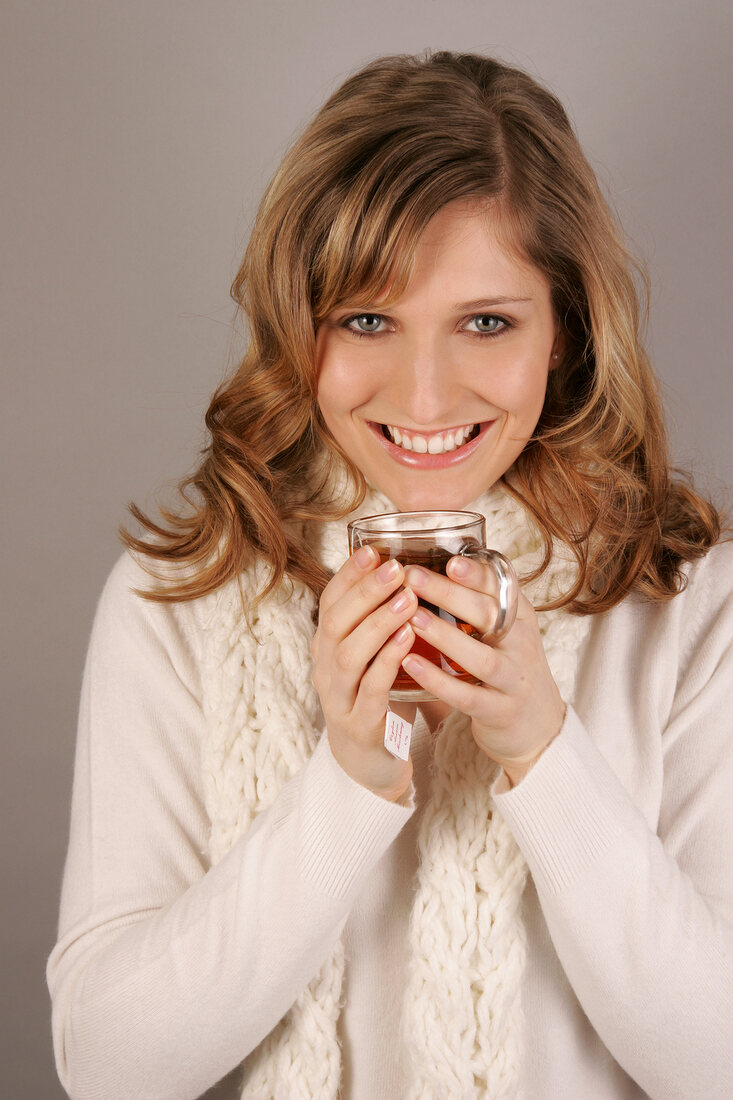 Woman with long hair wearing white sweater holding tea cup, smiling
