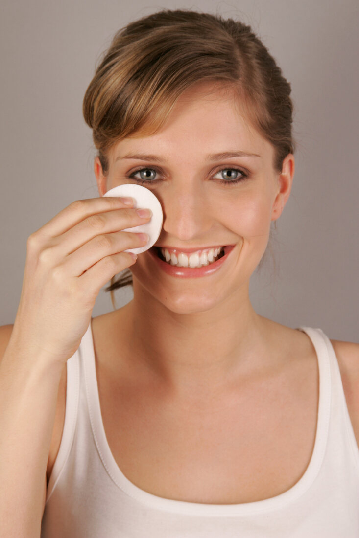 Portrait of pretty blonde woman cleansing her face with cleansing pad, smiling