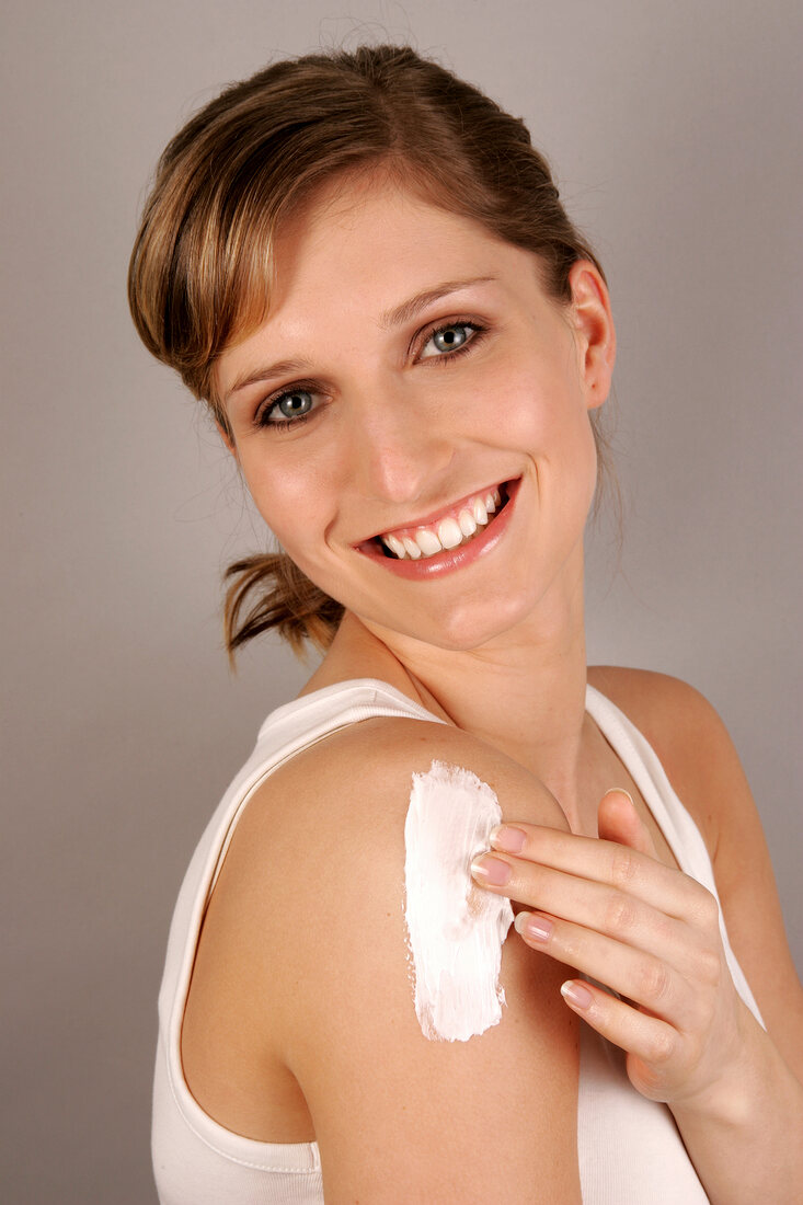 Portrait of gray eyed Charlotte woman with blonde hair applying cream on her arm, smiling