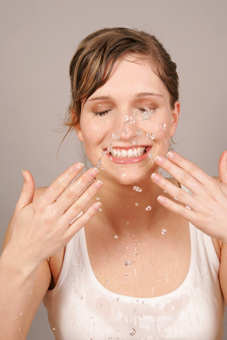 Pretty blonde woman having fun while splashing water on her face, smiling with eyes closed