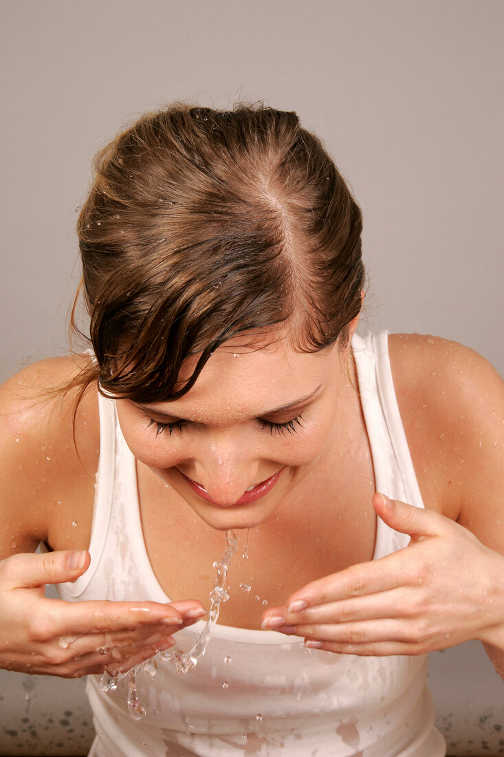 Pretty blonde woman having fun while splashing water on her face, smiling with eyes closed