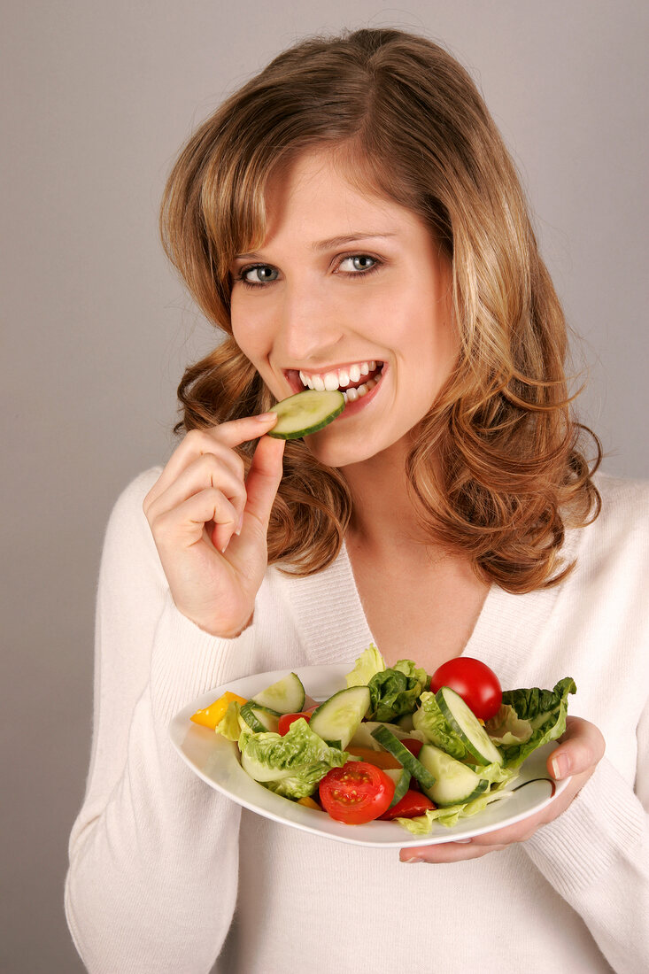 Portrait of beautiful woman eating cucumber slice while holding salad plate