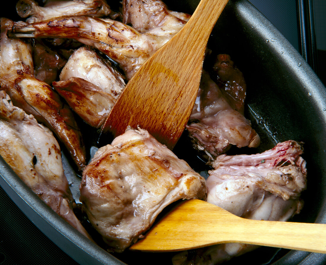 Pieces of brown rabbit meat in cooking pot with wooden spoon
