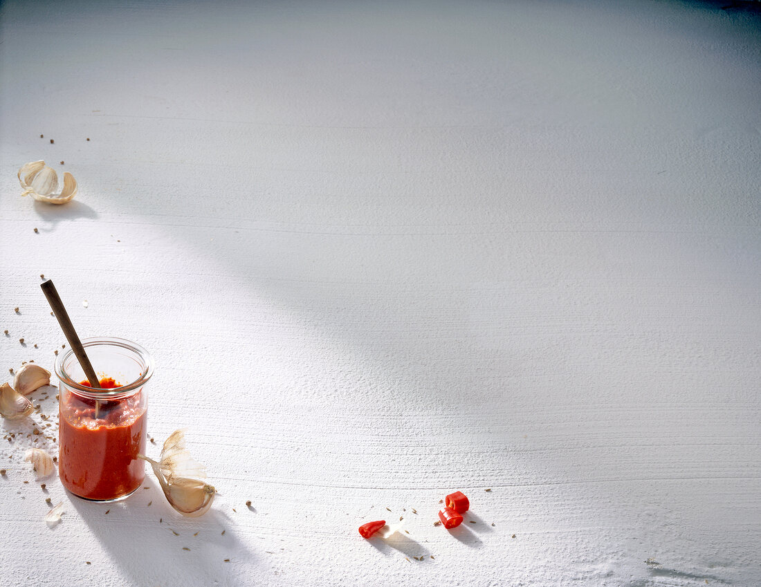 Glass jar of pepper sauce and garlic on white background