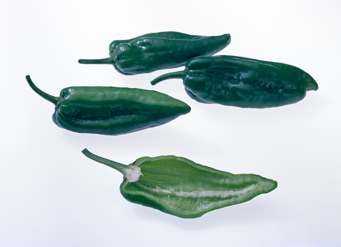 Halved and whole green peppers on white background