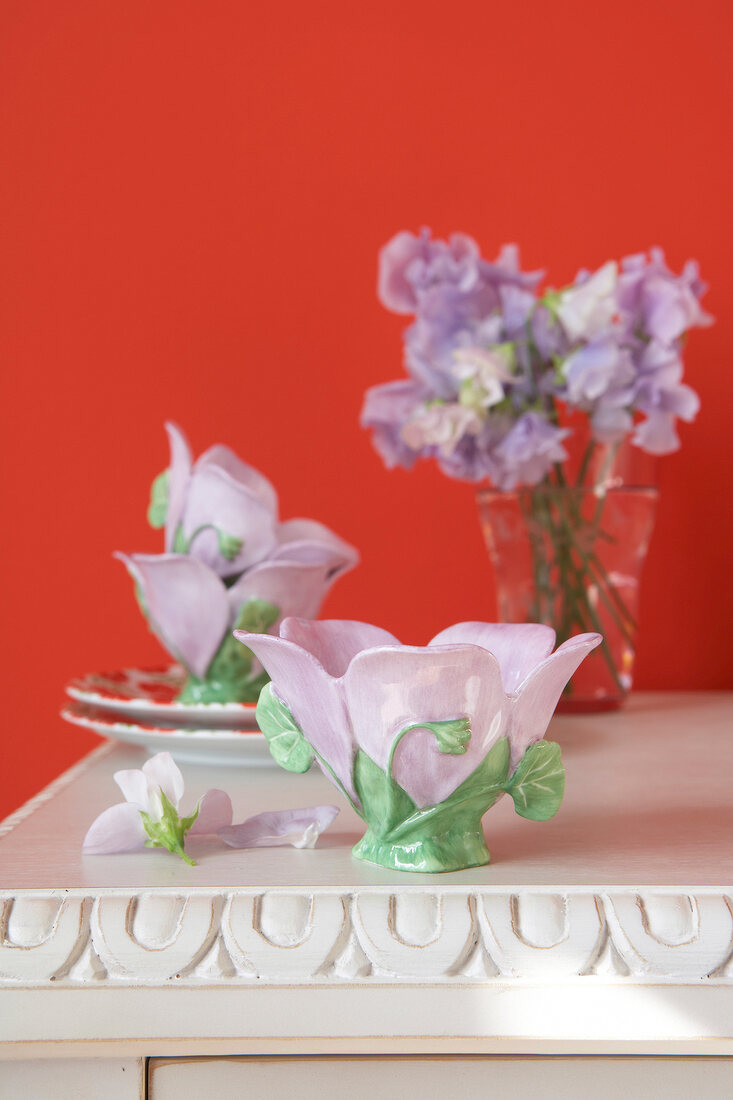 Close-up of flower shaped porcelain bowl with purple flower vase against red background