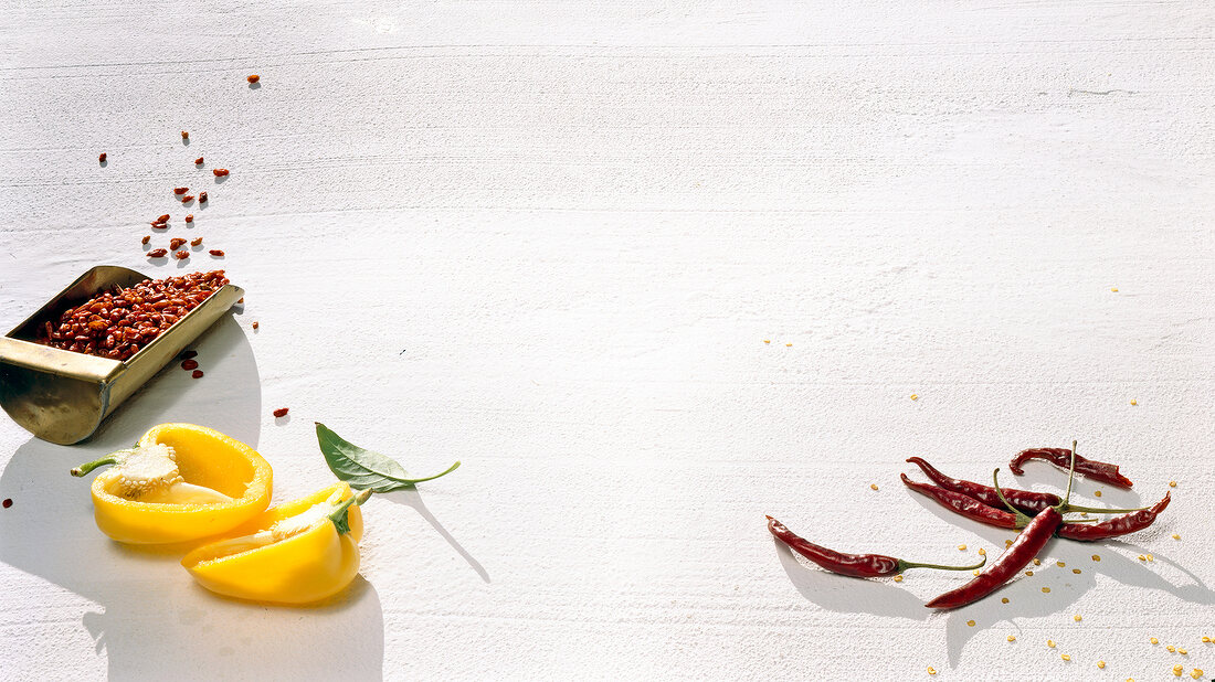 Halved yellow bell peppers and red chillies on white background
