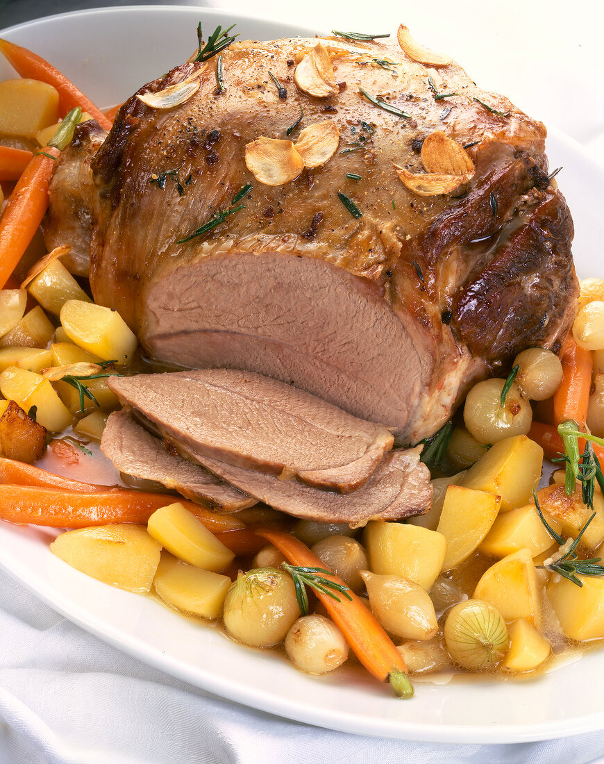 Close-up of leg of lamb with carrots, garlic and rosemary on plate