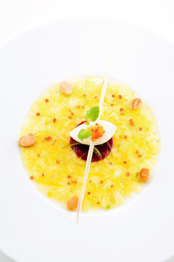 Close-up of pineapple carpaccio marinated in lemongrass oil with candied peppers