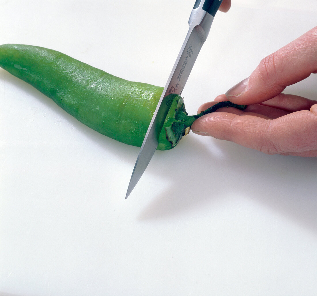 Stem of chilli pepper being cut with knife, step 1