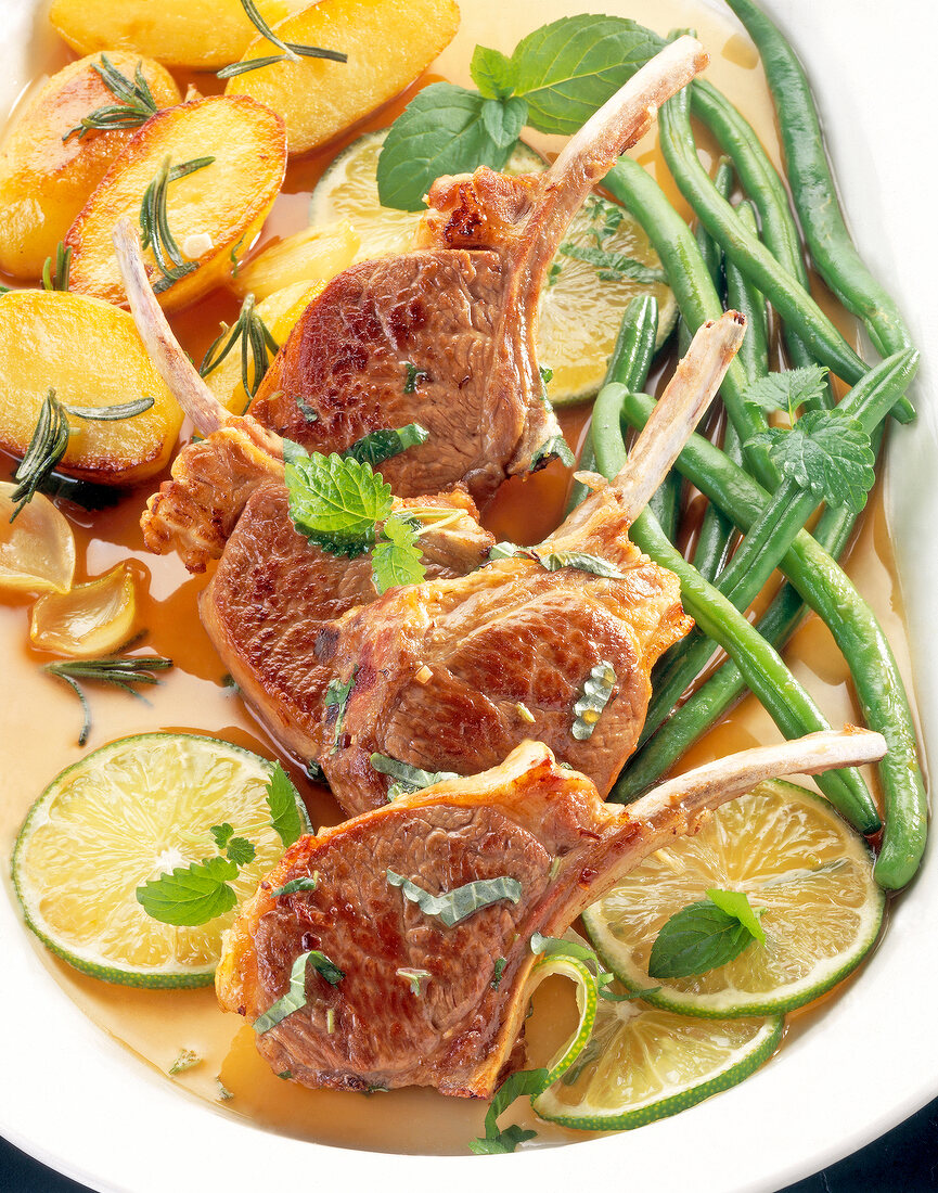 Close-up of lamb chops with green beans, rosemary potatoes and limes on serving dish