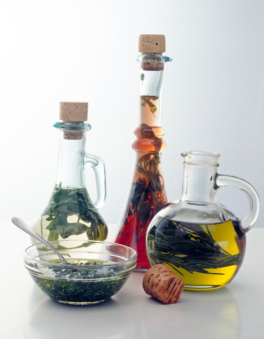 Glass bottles with oils and bowl with herbs against white background