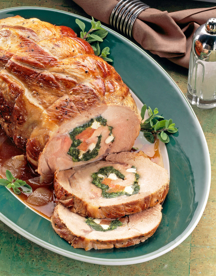 Slices of pork with spinach, sauce and herbs on serving dish