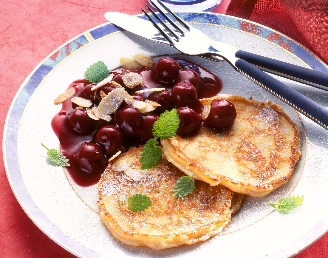 Quark pancakes garnished with cherry compote and herb on plate
