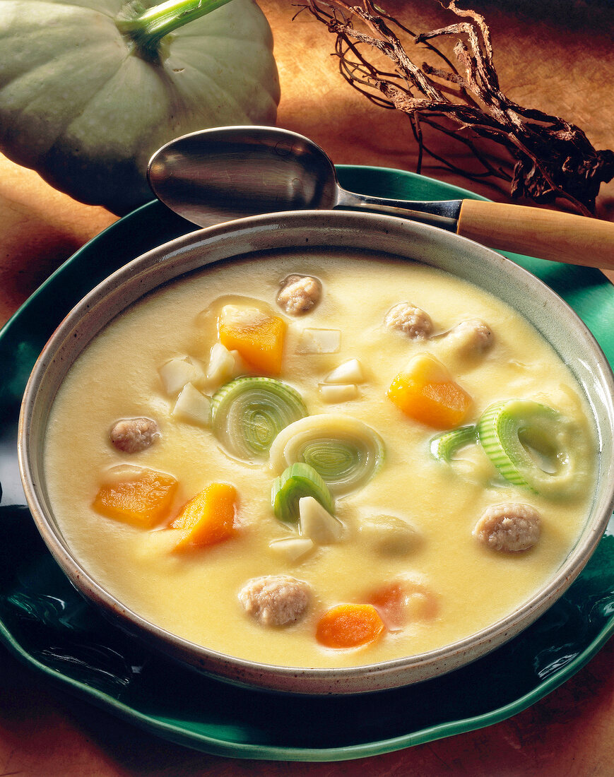 Pumpkin and potato cream soup with meatballs and leek on plate