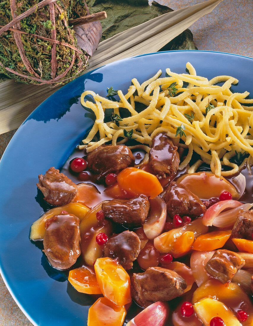 Close-up of wild boar goulash with apples and pasta on plate