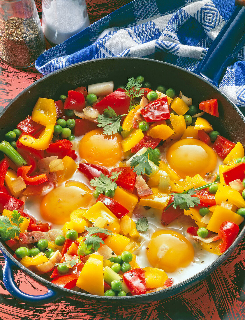 Close-up of egg and stir-fry vegetables with bacon, peppers and peas in pan