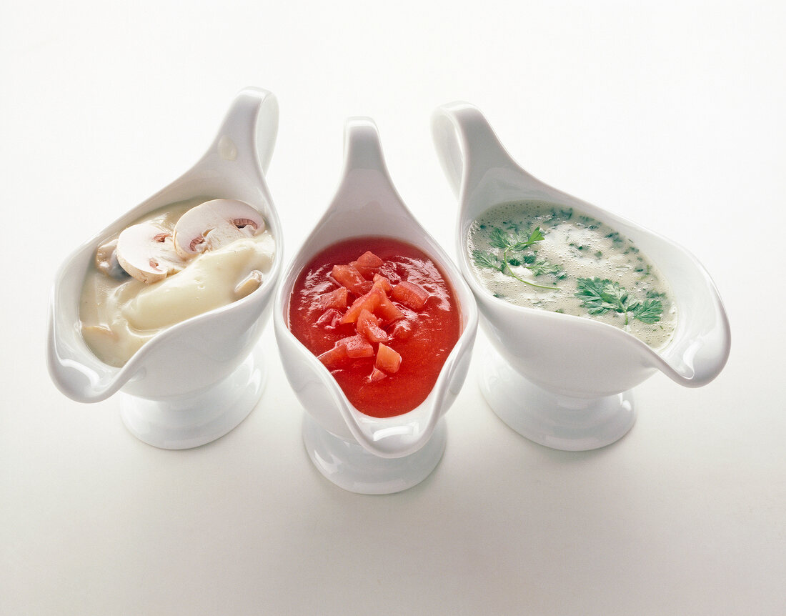 Three types of pasta sauce in sauce boats on white background