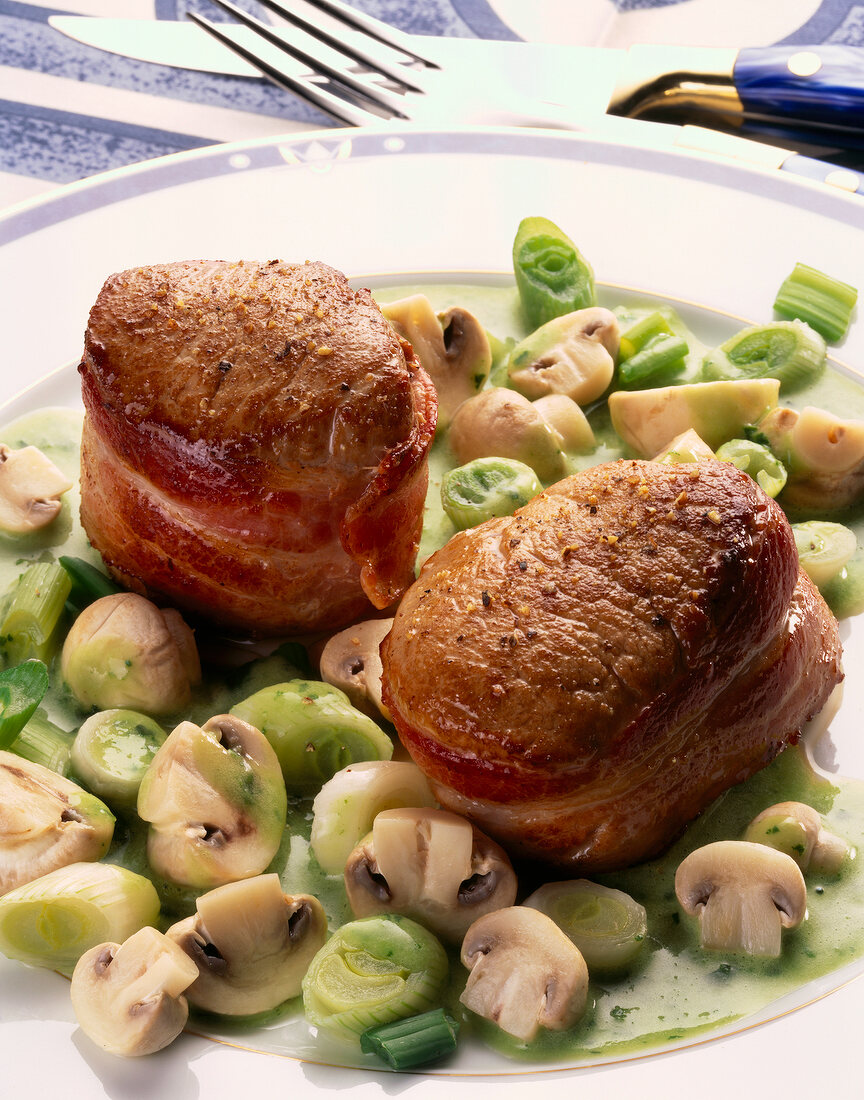 Close-up of pork medallions with mushrooms and chopped spring onions on plate