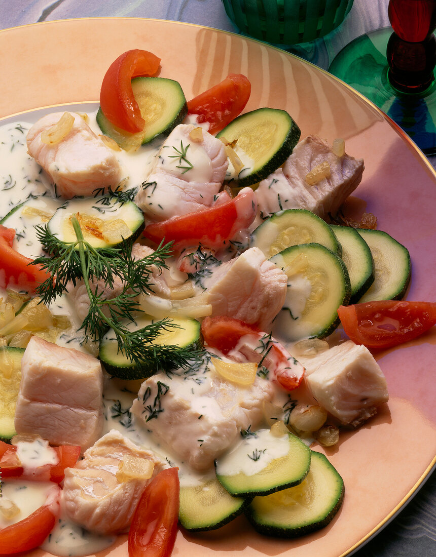 Close-up of fish stew with zucchini, tomatoes and dill on plate